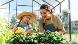 Happy mother and daughter are gardening in the greenhouse. Child is helping her mom and learning about botany.
