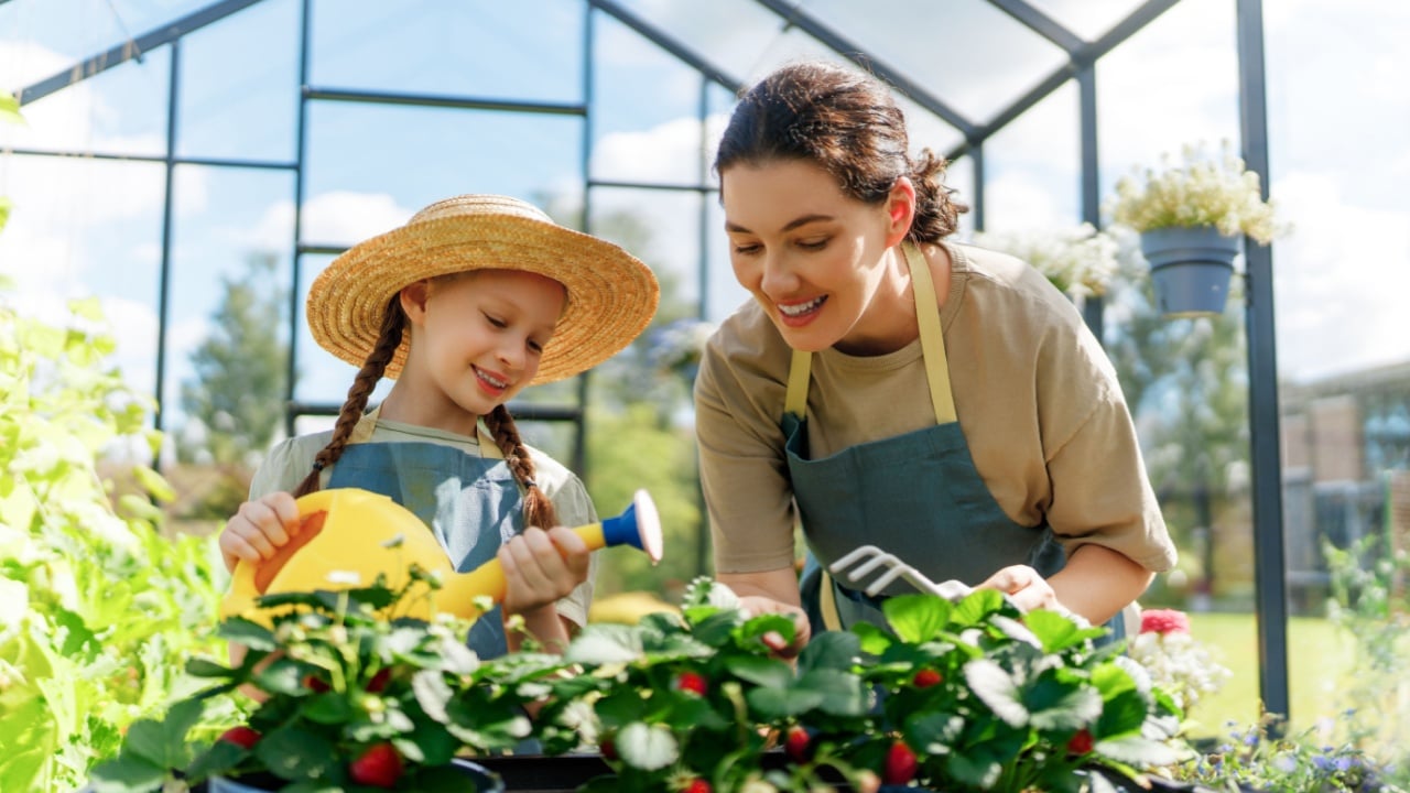 Happy mother and daughter are gardening in the greenhouse. Child is helping her mom and learning about botany.