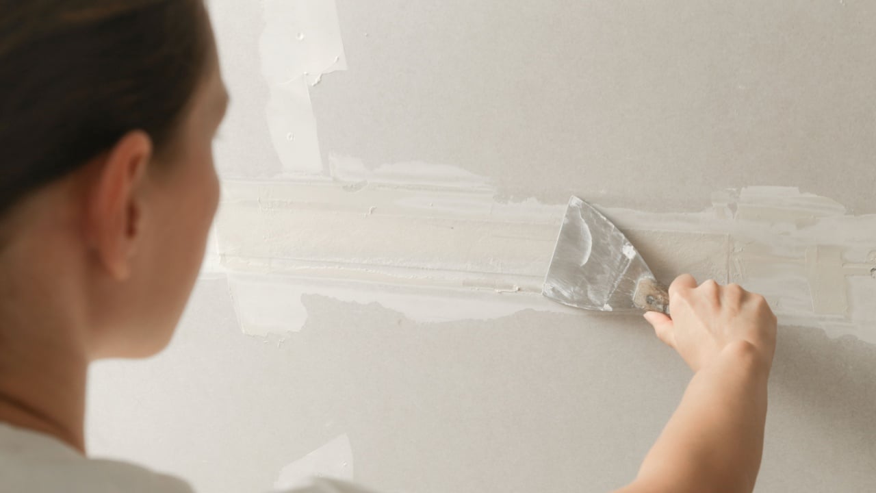 Woman taping and mudding joins pieces of drywall into a single solid wall. Fixing dry wall surface and preparation for painting. DIY housing improvement project.