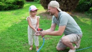Father holding hose while his daughter drinking water in backyard