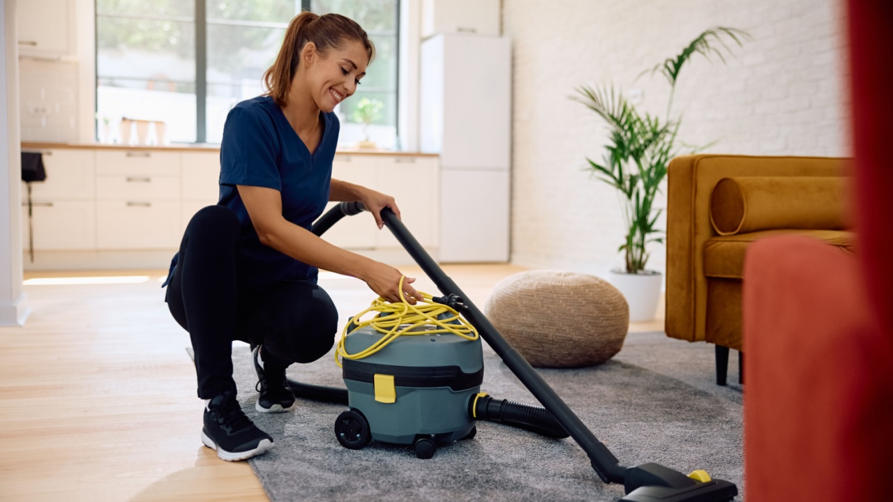 Happy woman using professional vacuum cleaner while cleaning apartment.