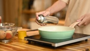 Close up woman spraying cooking oil onto frying pan on stove