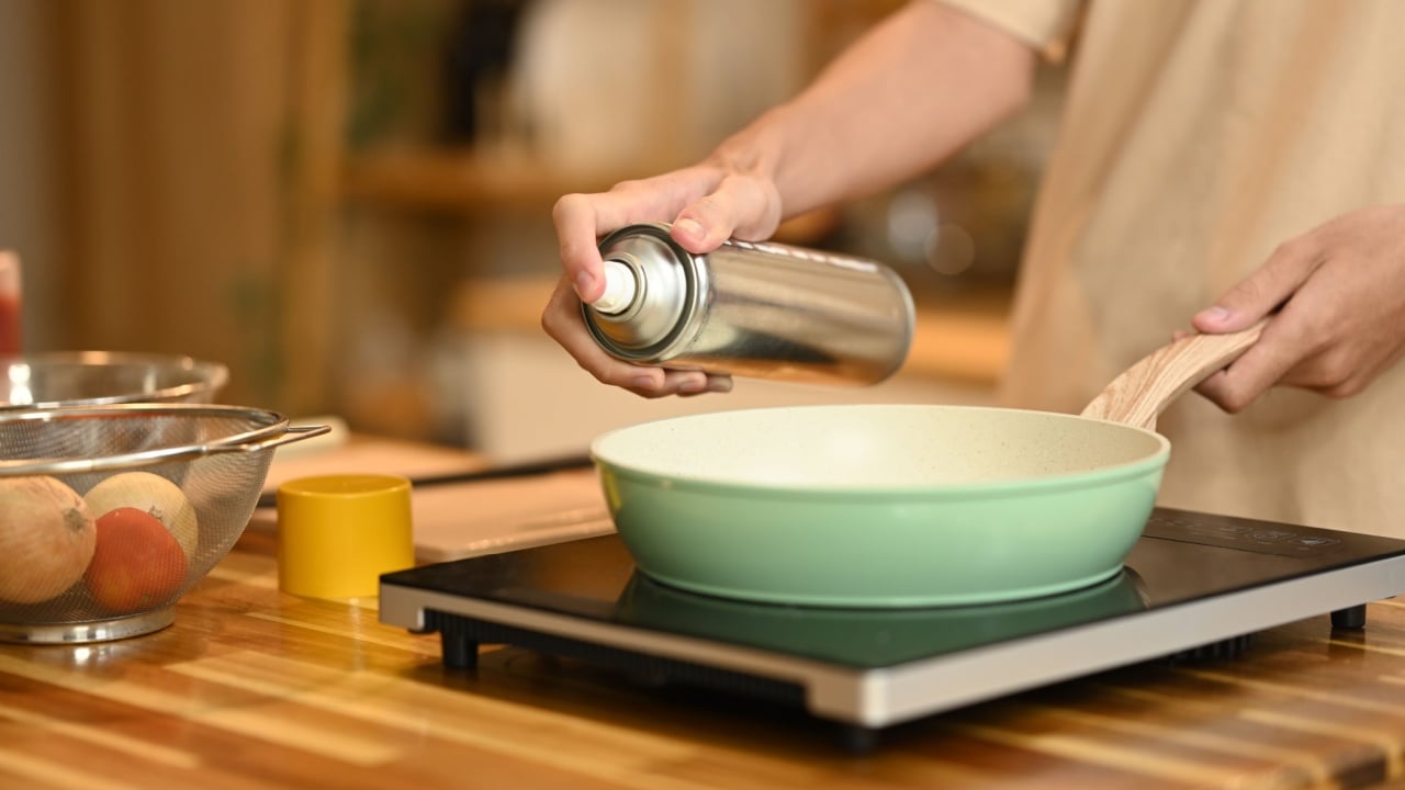 Close up woman spraying cooking oil onto frying pan on stove