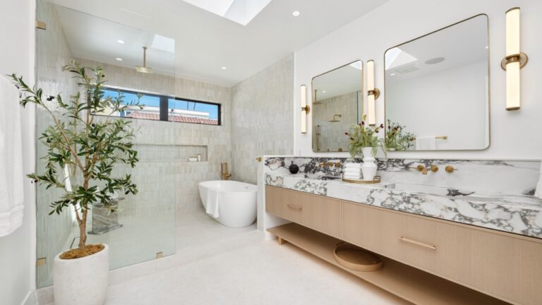 Modern luxury bathroom with marble countertop, large mirrors, and natural light from skylight, featuring a potted plant and elegant fixtures.