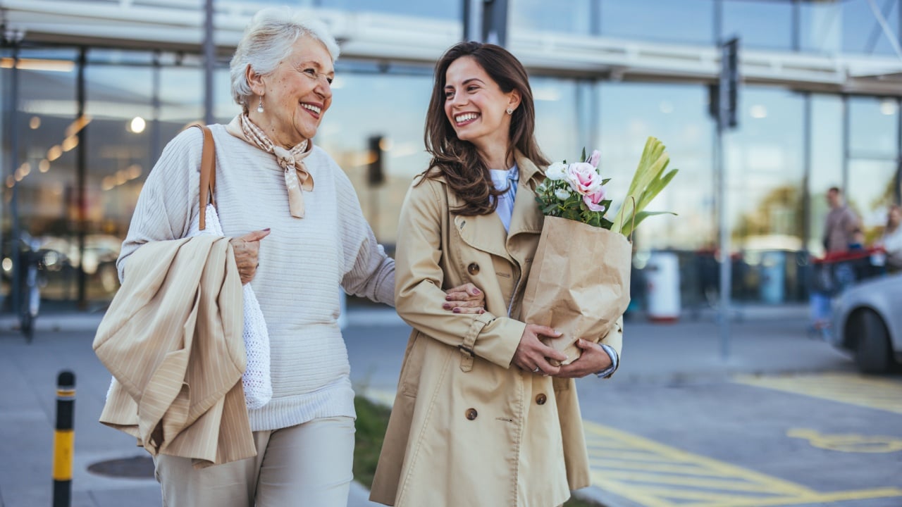 A joyous moment between a smiling mother and daughter as they shop together. They are walking arm in arm with flower bouquet, displaying love and companionship.