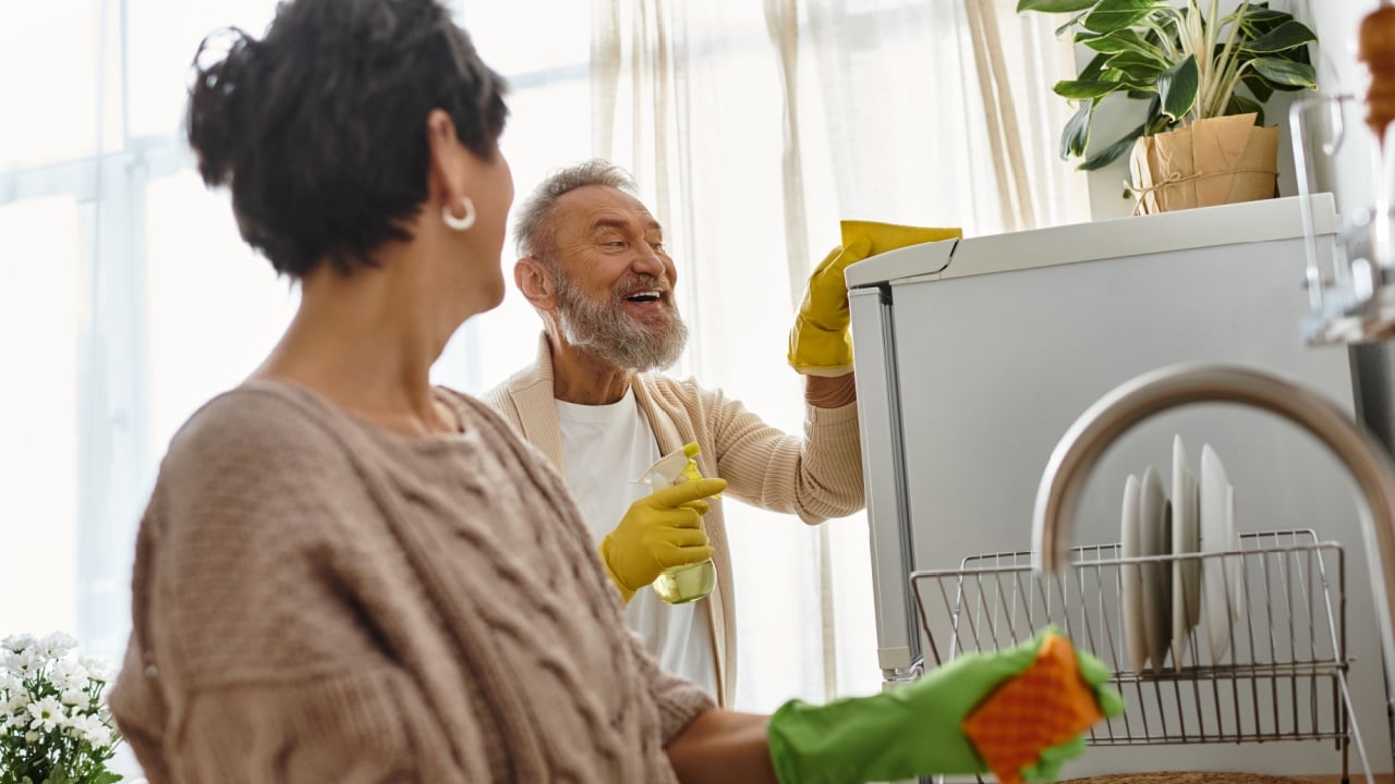 A cheerful couple enjoys their time cleaning the kitchen, sharing smiles and laughter.