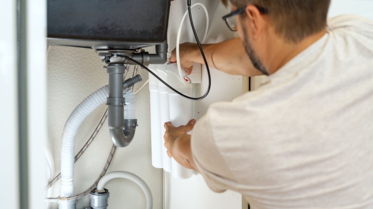 Replacement water purifier. Plumber installs water filter and changes water filter cartridges in kitchen under kitchen sink