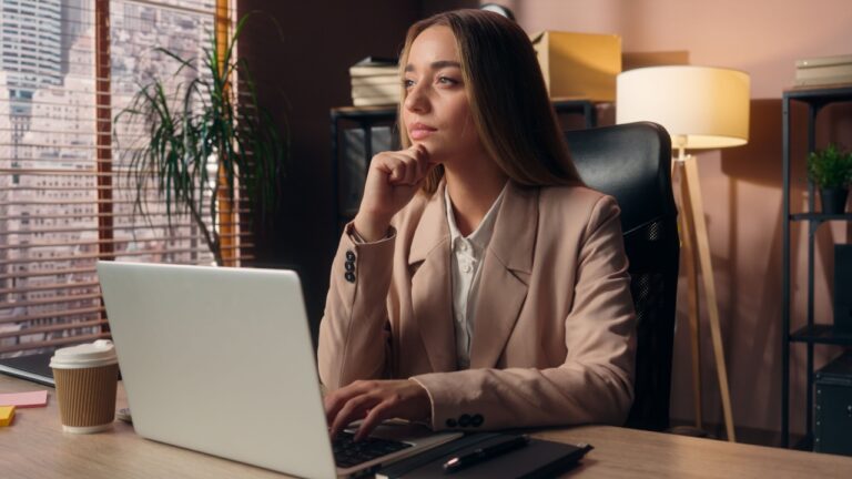 Confident dreamy successful Caucasian business woman female lawyer entrepreneur girl businesswoman office worker agent working computer typing laptop brainstorming thinking daydreaming ponder indoors