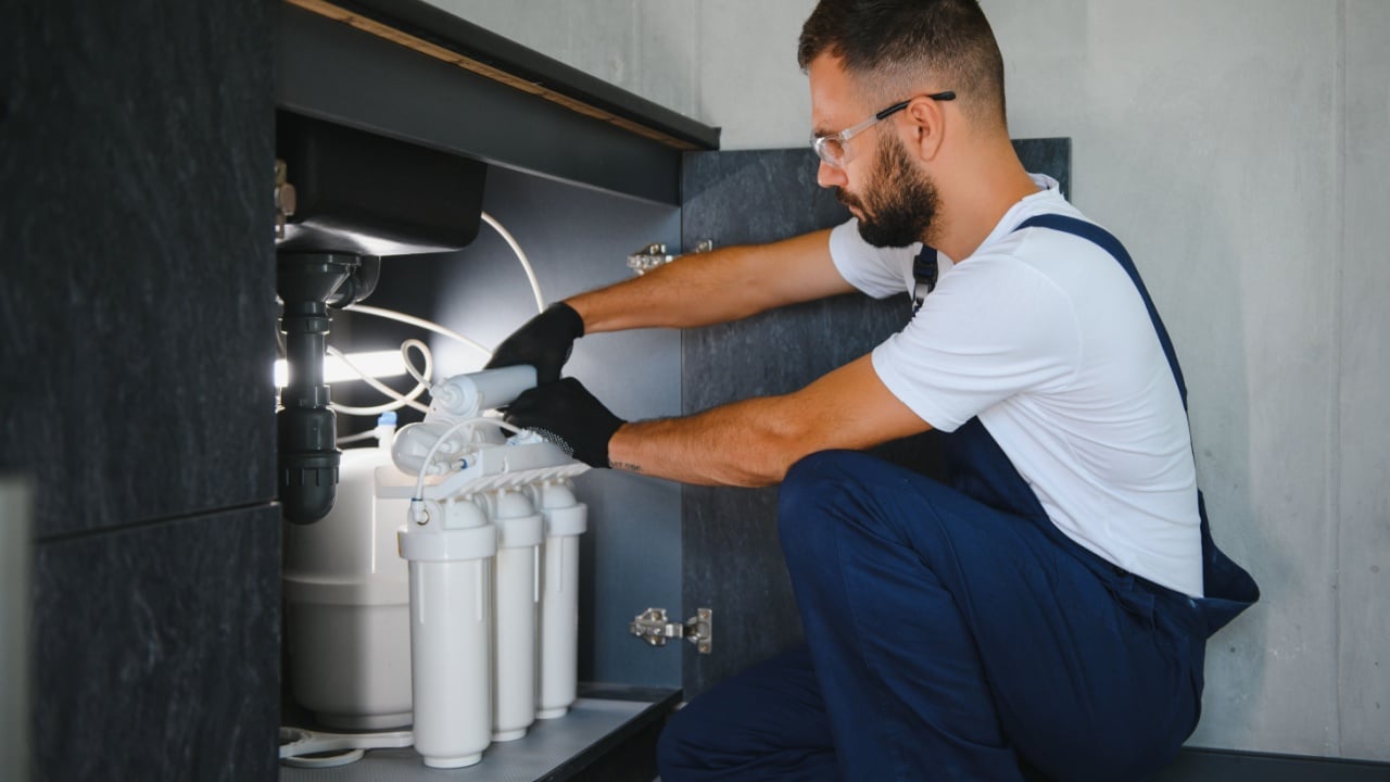 Plumber installs or change water filter. Replacement aqua filter. Repairman installing water filter cartridges in a kitchen. Installation of reverse osmosis water purification system.