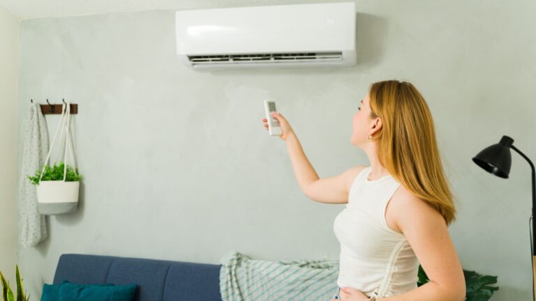 Young woman adjusting air conditioning temperature using remote control in her living room during summer heat