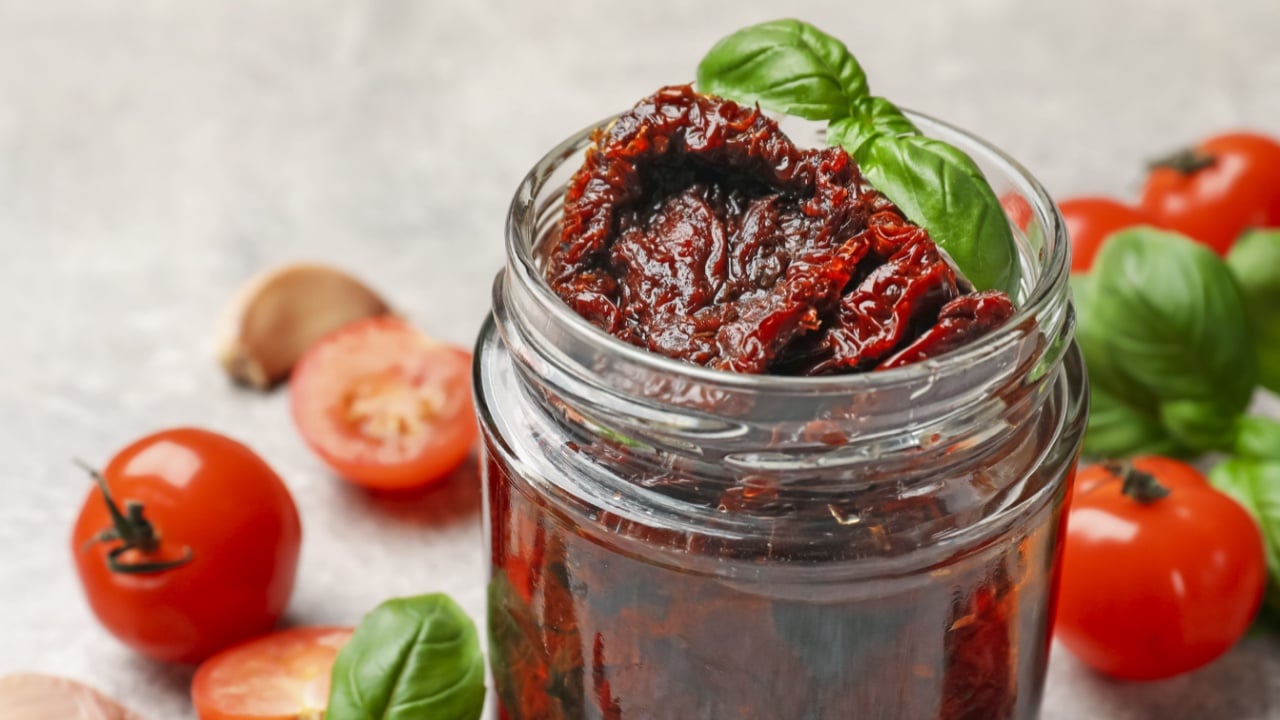 Delicious sun dried tomatoes, fresh vegetables, basil and garlic on light grey table, closeup