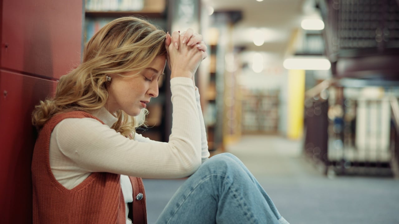 University, girl and stress on library floor for academic burnout, student loans or study fatigue. Education, anxiety and person with depression on campus for workload pressure or overwhelmed by exam