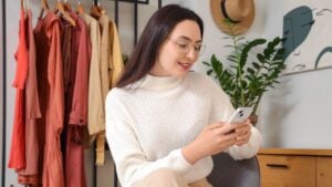 Young woman using mobile phone near clothes rack at home