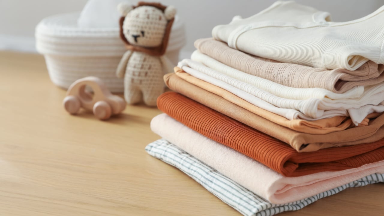 Stack of clean baby clothes and toys on wooden table indoors, closeup