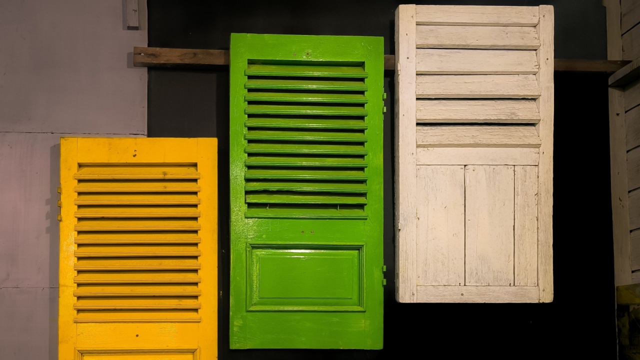 three old wooden window shutters mounted on a wall as decoration. Each shutter is painted in a different color: bright yellow on the left, vibrant green in the middle, and worn-out white on the right.