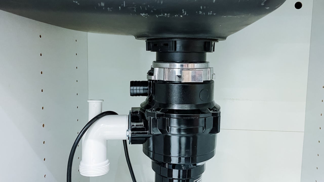 Beneath the kitchen sink, there exists a garbage disposal unit that is designed to efficiently shred food waste into tiny particles, making it easier to wash down the drain and maintain cleanliness