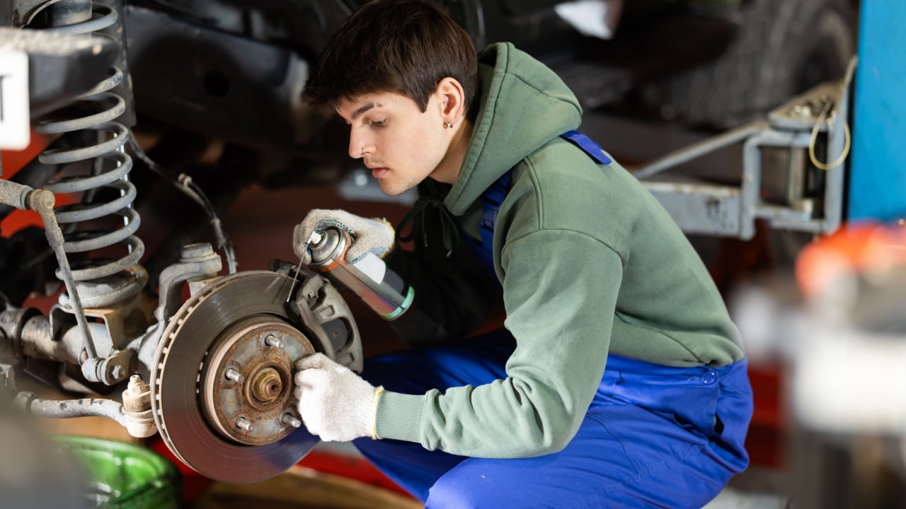 Auto mechanic applying anti-rust liquid to bolts on car wheel hub