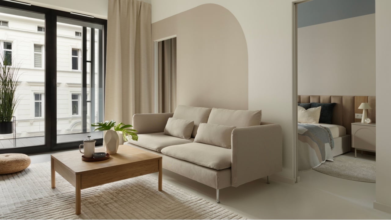 Contemporary living room with beige sofa, wooden coffee table and large window with curtains.
