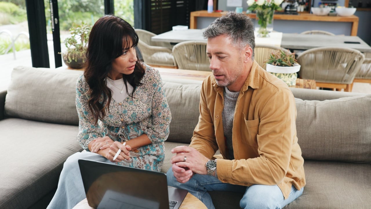 Couple, talking and sofa with laptop at house for planning, review budget and online payment. Mature people, discussion and pc for household expenses, financial savings and loan application for bills