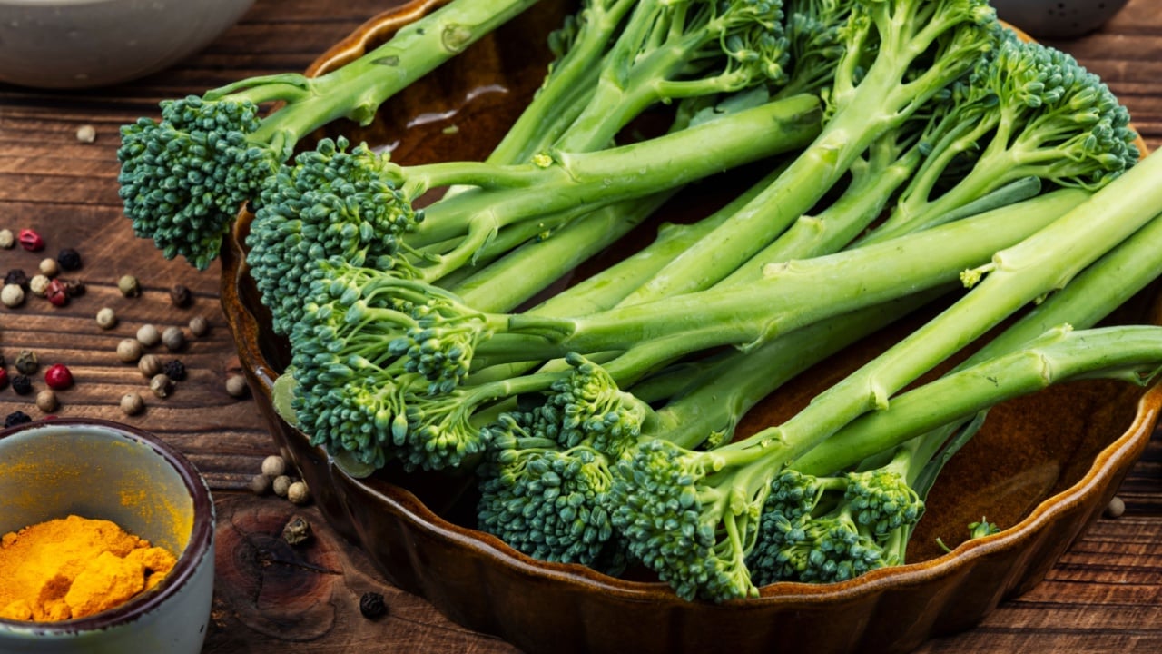 Green broccoli stalks surrounded by bowls, herbs, and spices, emphasizing fresh cooking ingredients.