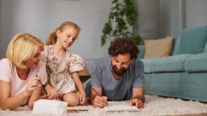 Family members engage in a fun drawing activity on a soft rug in a bright living room. Parents and child share joy, expressing creativity with smiles and laughter.