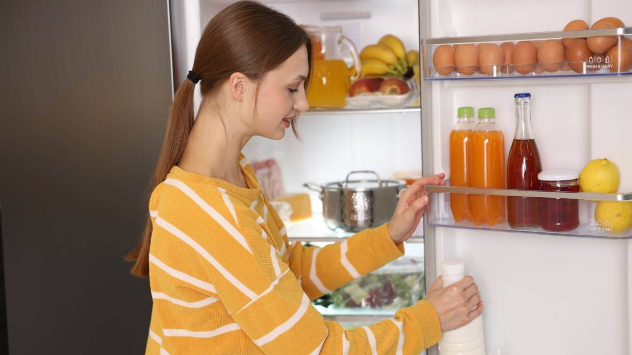 Woman taking bottle of milk from refrigerator in kitchen