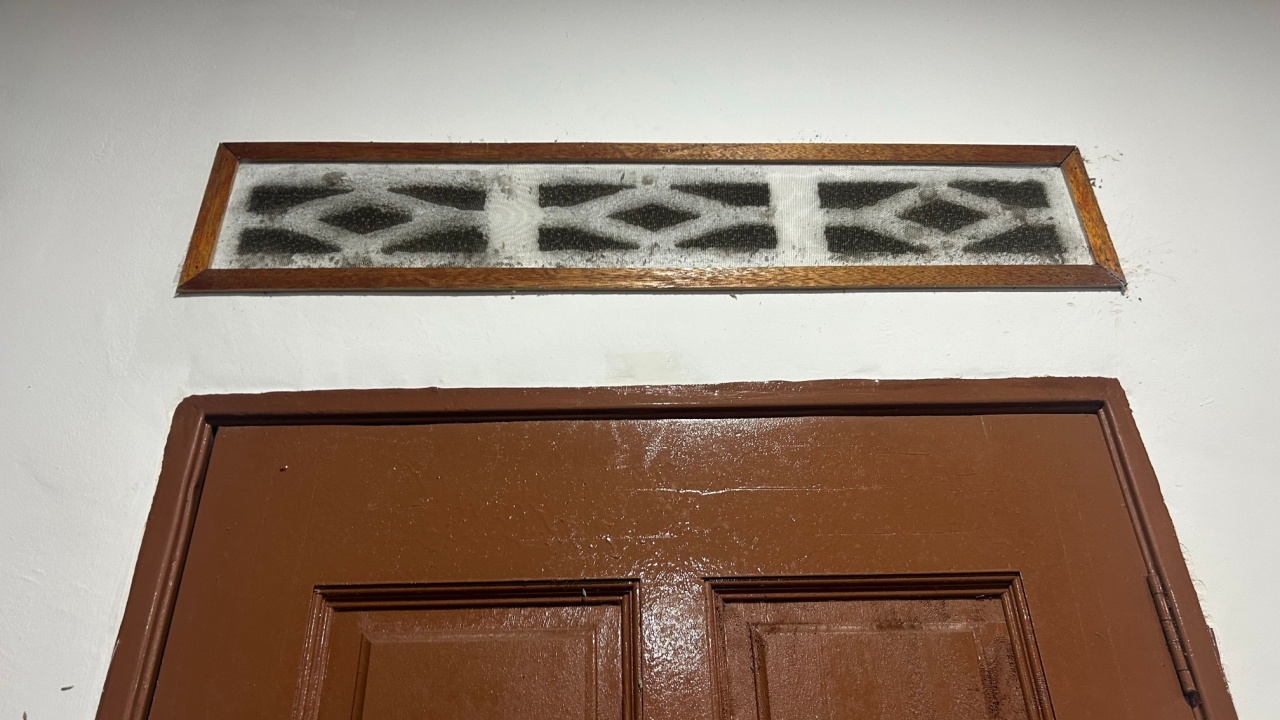 Low angle view of a vintage wooden door with a decorative patterned transom window for ventilation in a traditional Southeast Asian home