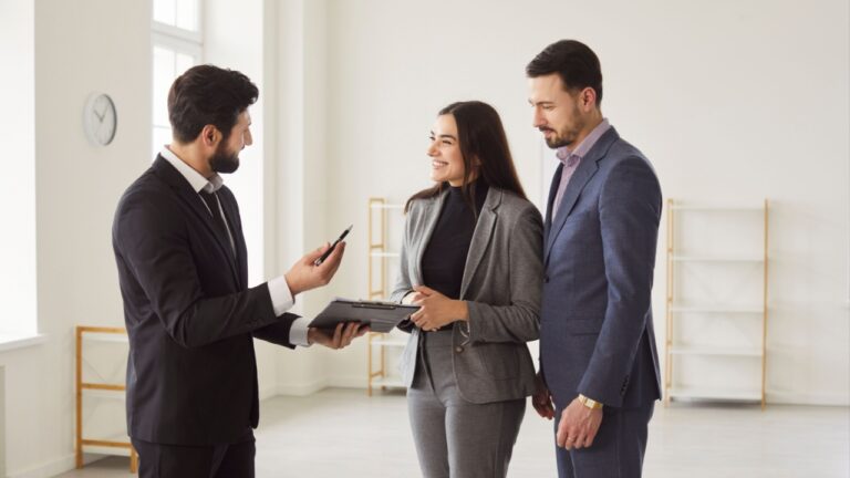 Young happy smiling couple reaching agreement with man realtor and looking through the contract of real estate sale and going to sign a contract. Real estate market and buying a property concept.