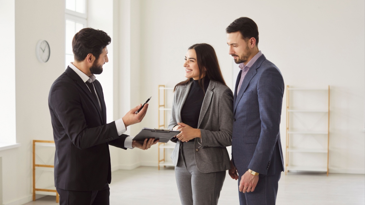 Young happy smiling couple reaching agreement with man realtor and looking through the contract of real estate sale and going to sign a contract. Real estate market and buying a property concept.