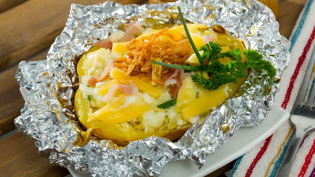 Tasty cooked in foil baked potato filled of salad with cheese, bacon and fried onion..