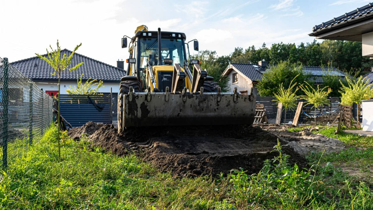 Backhoe loader moving soil for ground leveling in a residential backyard
