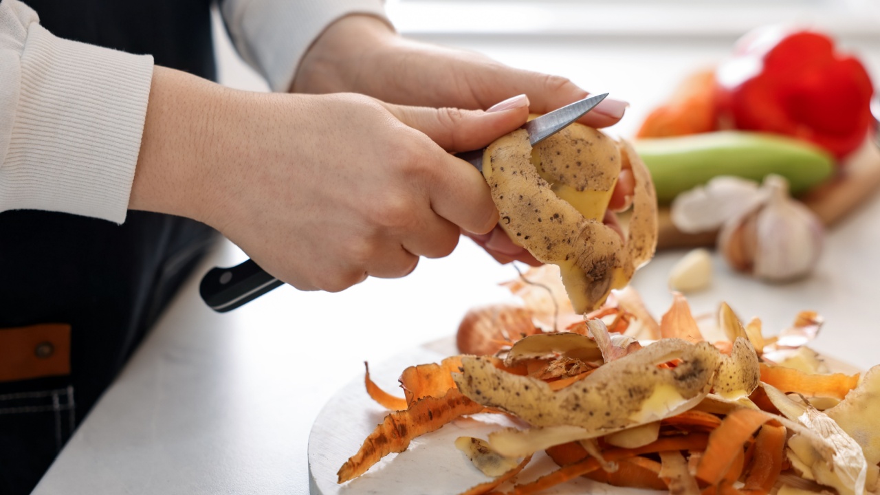 Woman peeling fresh potato at light table with leftovers and vegetables indoors, closeup