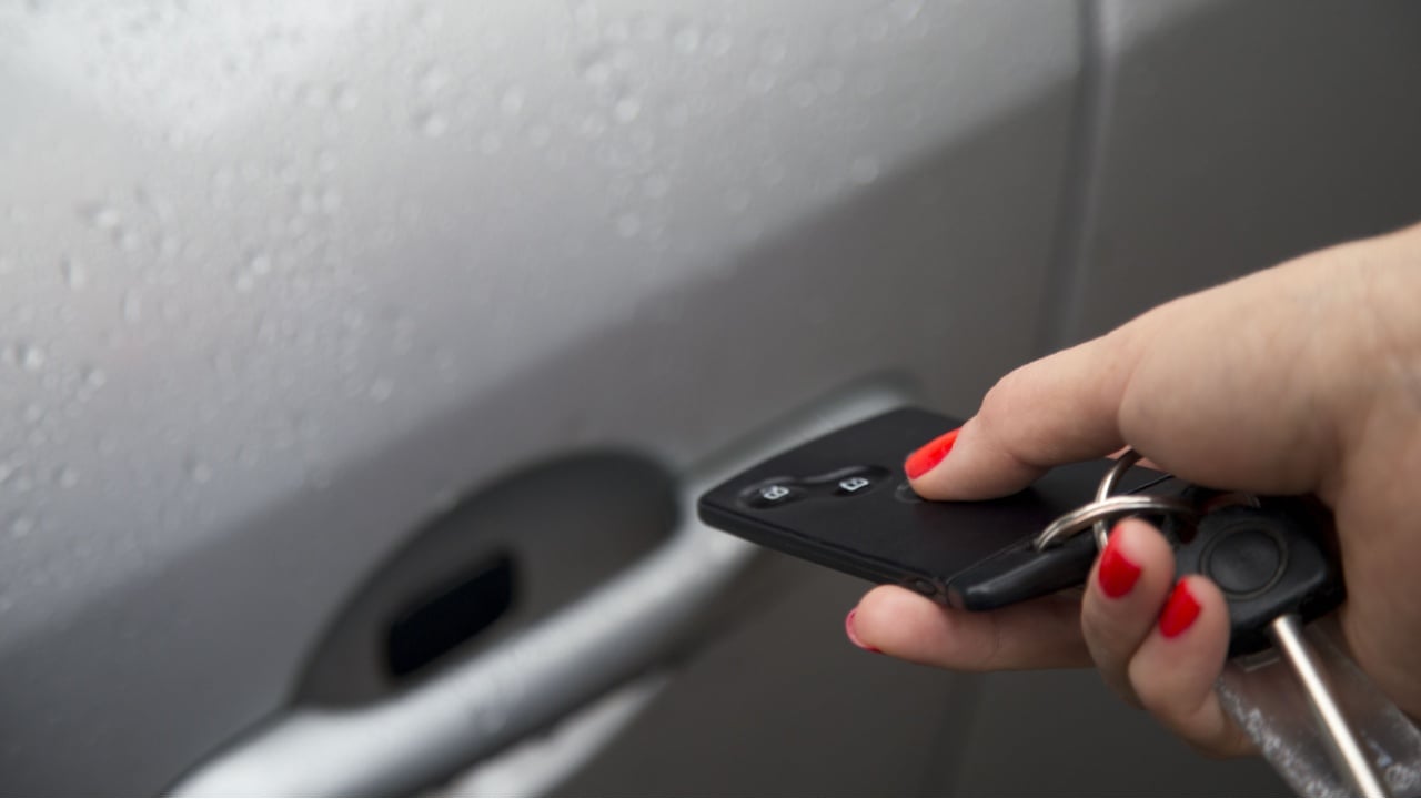 Woman using central locking remote key to open car door. Locking car door.