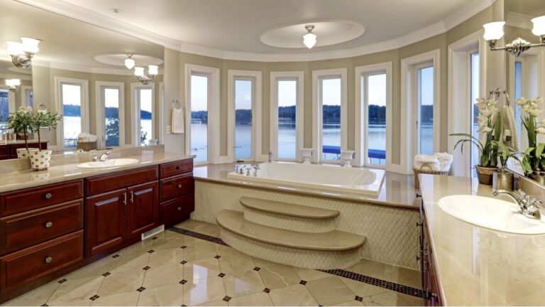 Luxurious master bathroom interior boasts jetted tub with curved windows facing the lake, two cherrywood vanity cabinets facing each other and glossy marble floor. Northwest, USA