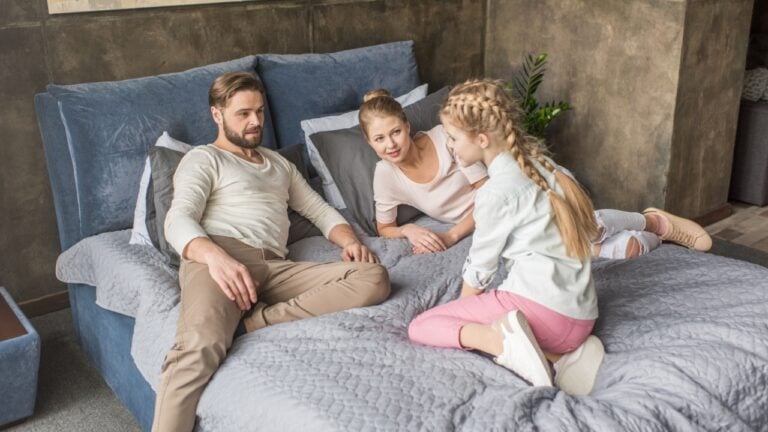 happy adorable daughter with mother and father relaxing on bed at home