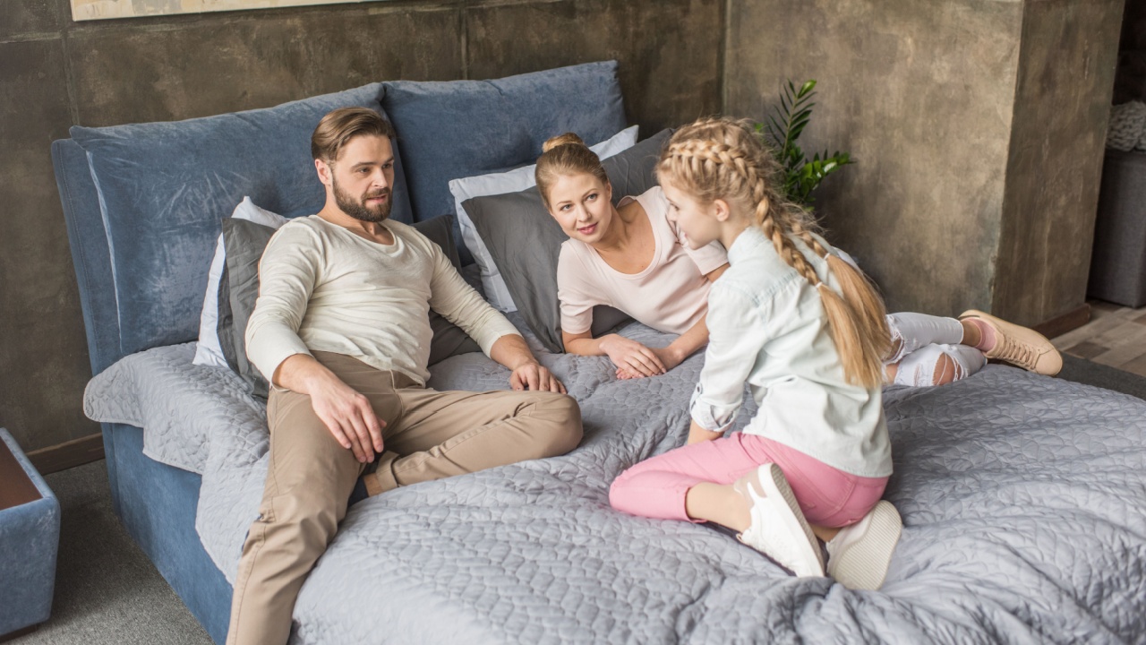 happy adorable daughter with mother and father relaxing on bed at home