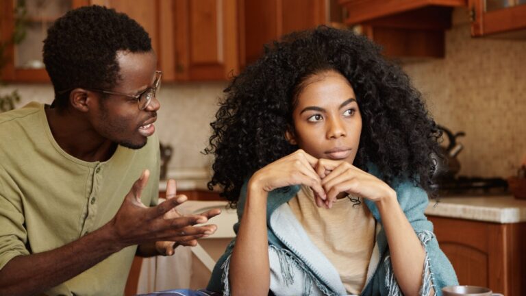 Furious black male gesturing in despair or anger while trying to make excuses to his offended wife as if saying: Can you just hear me out? African couple going through hard time in relationships