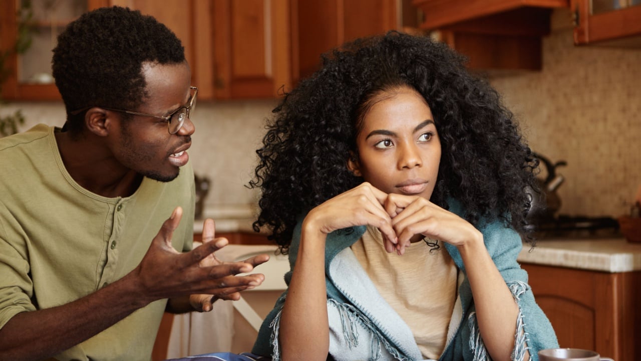 Furious black male gesturing in despair or anger while trying to make excuses to his offended wife as if saying: Can you just hear me out? African couple going through hard time in relationships