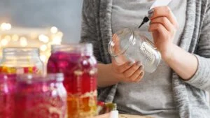 Young woman decorating DIY jars with paint