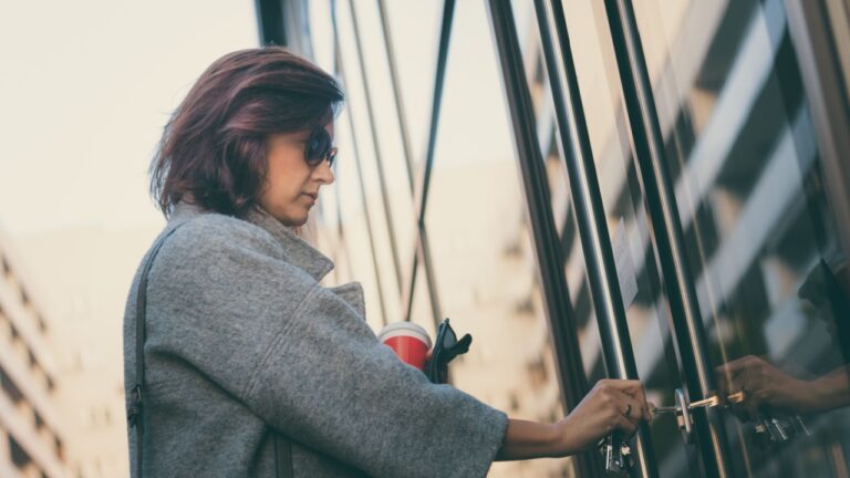 Beautiful woman unlocking door with a key and entering in residential building.