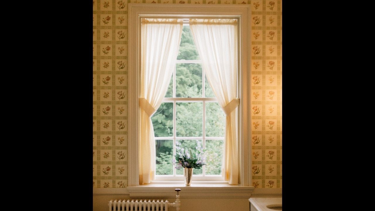 A vintage bathtub rests beneath a window with sheer curtains, providing a serene view of lush greenery outside.