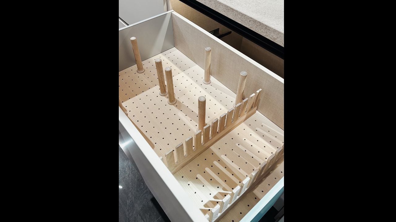 Open kitchen drawer with a modern wooden peg and movable divider storage for home organization.