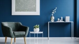 Green armchair against the wall with silver painting in navy blue living room interior with flowers