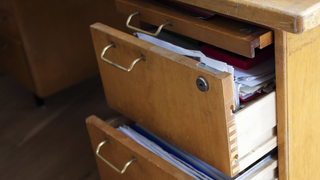 Closeup photo of old wooden desk with half-open drawers filled with papers.