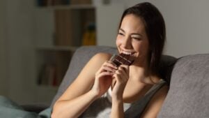 Woman enjoying eating chocolate in the night sitting on a couch in the living room at home