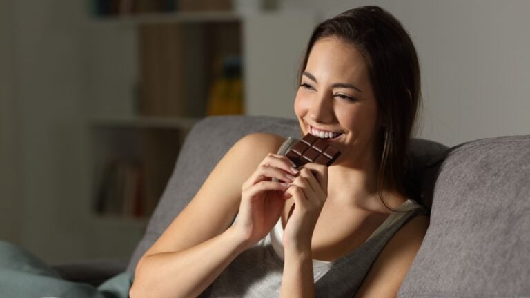 Woman enjoying eating chocolate in the night sitting on a couch in the living room at home