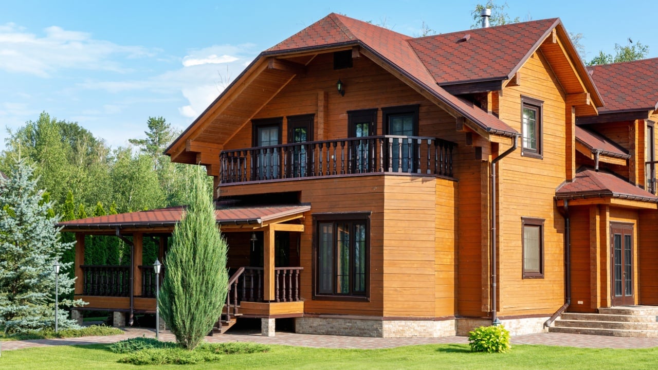 Beautiful luxury big wooden house. Timber cottage villa with with green lawn, garden and blue sky on background