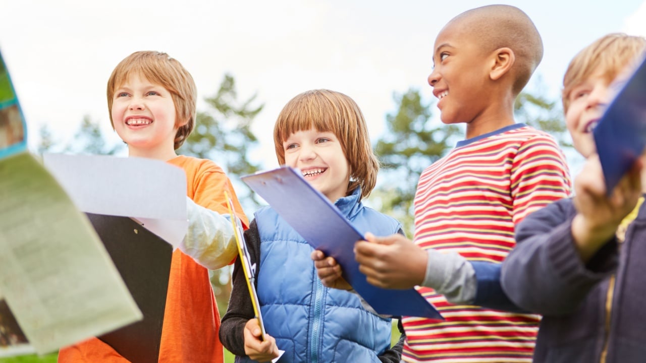 Happy children on a treasure hunt as a scavenger hunt in nature with clipboard