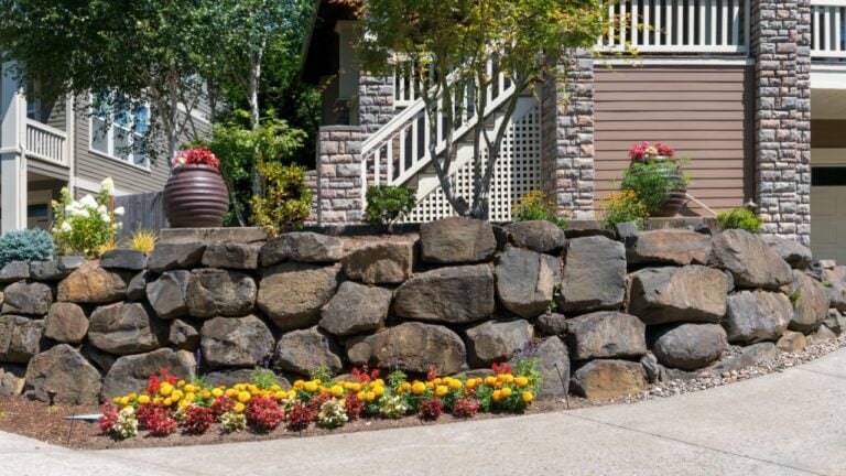 House front yard garden landscaping with cut rocks retaining wall stone works facade with potted plants and flowers