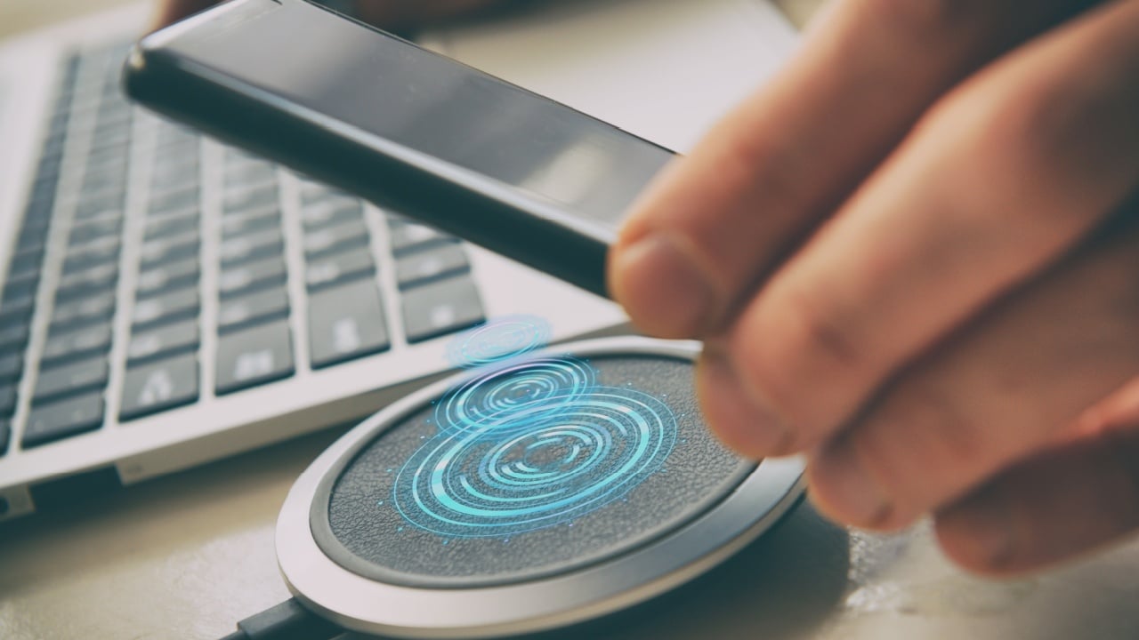 Smartphone in hand near a wireless charging pad, charger.